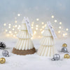 Two white layered Christmas tree candles with brown bases and decorative tags, surrounded by silver and gold baubles on.