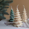 Set of three pine tree-shaped candles in cream and dark green with textured branches.