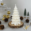 White pine tree-shaped candle on wooden slice base surrounded by pinecones and gold ornaments.