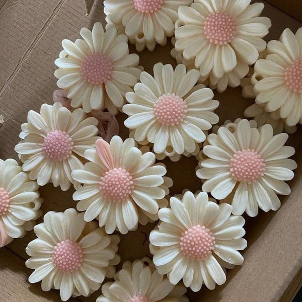 Cream-colored daisy candles with pink textured centers arranged in a cardboard box.