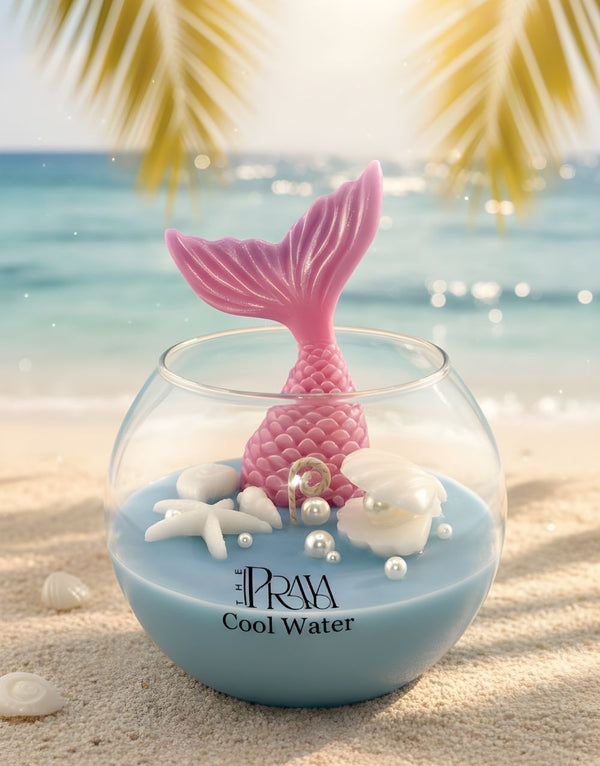 Round glass jar candle with blue wax, pink fish tail wick, and seashell decorations labeled "ARIA Cool Water".