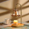 Brass electric candle warmer lamp with amber glass shade over lit candle on wooden base.