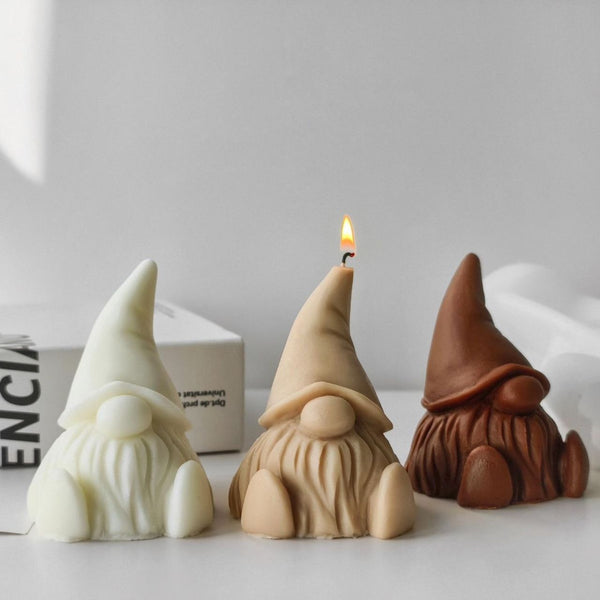 Three gnome-shaped soy wax candles in cream, beige, and brown colors, one lit in the center.