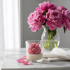 Glass jar candle with pink lotus flower-shaped wax design on white marble surface.