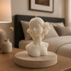 Ivory candle shaped as a bust of a woman with flowers in her hair, placed on a round stone base on a wooden table.
