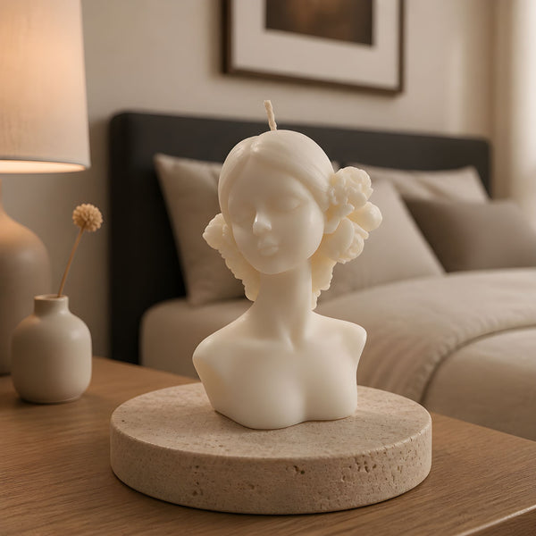 Ivory candle shaped as a bust of a woman with flowers in her hair, placed on a round stone base on a wooden table.