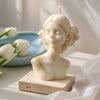 Cream-colored lady bust candle with floral hair details on a square stone base.