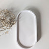 Matte white oval tray with raised edges on neutral background with dried flowers.