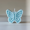 Light blue butterfly-shaped candle with detailed wing patterns and white wick on top.