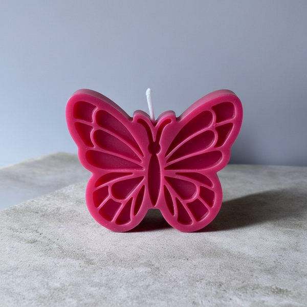 Pink butterfly-shaped candle with detailed cutout wing patterns and a centered wick.