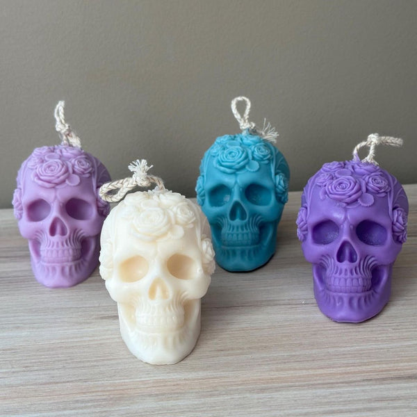 Four Halloween skull candles in purple, cream, teal, and violet with detailed bone texture and twisted wicks.