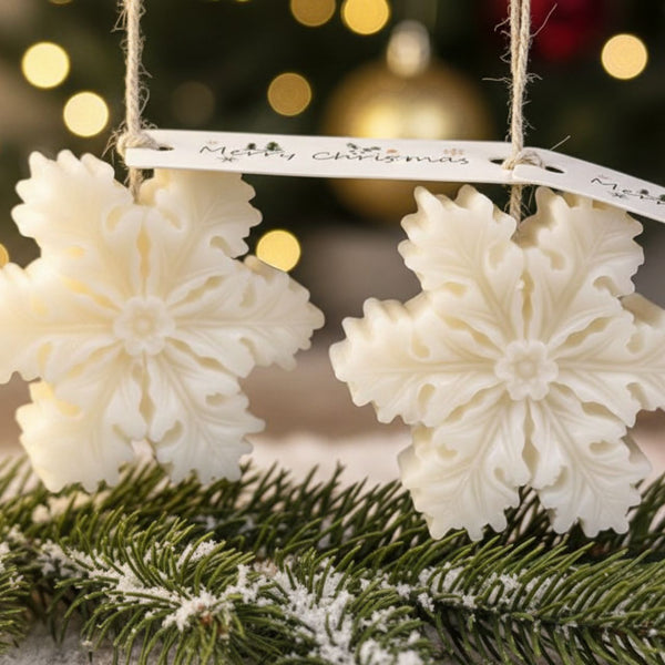 White snowflake-shaped candles hanging from rustic twine with a festive background and pine branches below.