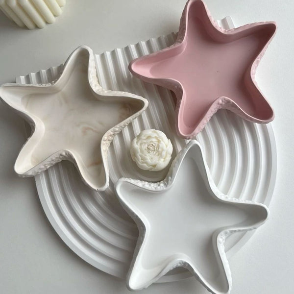 Set of three handmade star-shaped trays in beige, pink, and white ceramic on a ridged round white base with a small.