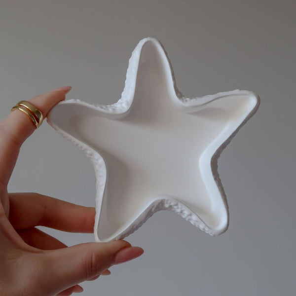 Handmade white ceramic star-shaped tray with textured edges held by a hand.