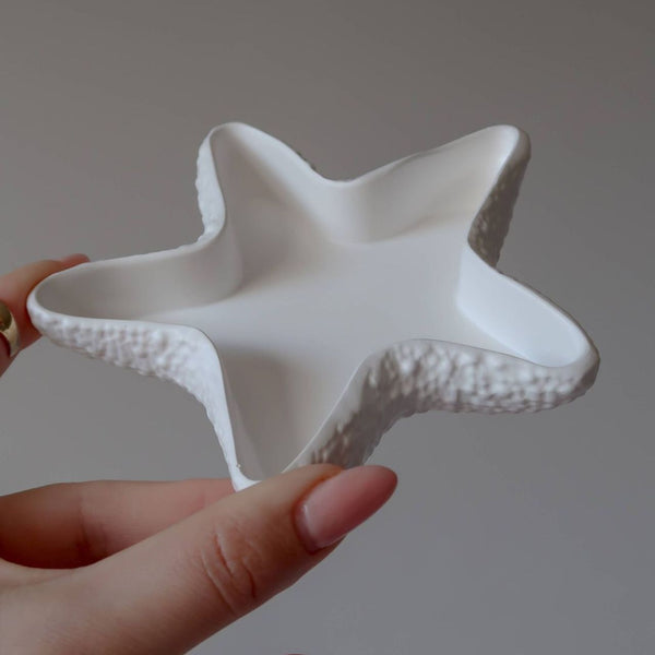 White handmade ceramic star-shaped tray with textured edges held in hand.