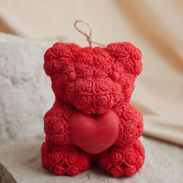 Red teddy bear candle made of detailed rose-shaped wax petals holding a solid red heart.