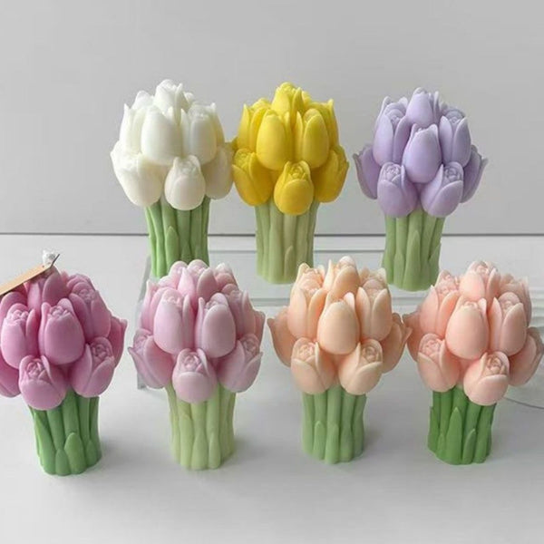 Seven tulip flower bouquet candles in white, yellow, purple, pink, peach, and lavender shades arranged on a flat surface.