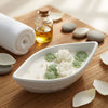 White ceramic candle with lotus-shaped wax melts and green leaf accents on wooden surface.