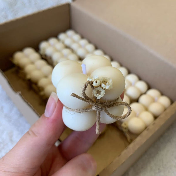 Hand holding a cream-colored bubble candle tied with a rustic twine bow in front of a cardboard box filled with similar.