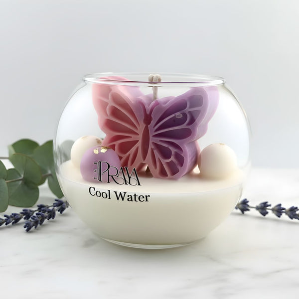 Round glass jar candle with a two-tone purple and pink butterfly-shaped wax centerpiece and white wax base labeled Cool Water.