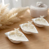 Three white soy wax candles shaped like conch shells with starfish details on a wooden surface with pampas grass in the.