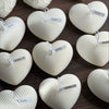 White heart-shaped candles with textured surface and small labels tied with string on wooden background.