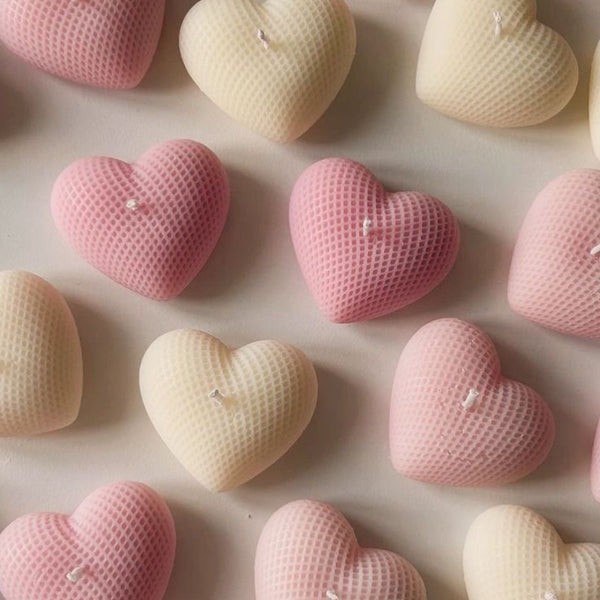 Pink and cream heart-shaped candles with textured surface arranged evenly on a beige background.