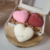 Set of three heart-shaped candles in pink, red, and cream with textured surface in an open gift box.