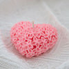 Pink heart-shaped candle covered with small detailed floral patterns on white fabric background.