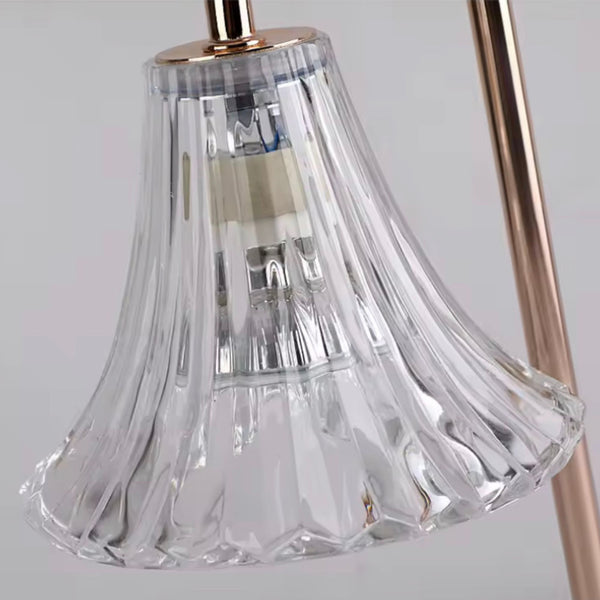 Clear ribbed glass lampshade with flared scalloped edge on metallic rose gold lamp arm.