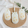 Set of three white soy wax hanging sachets with cream flower details and white ribbons on woven mat.