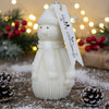 White snowman-shaped candle with knit hat and scarf, textured body, and "Merry Christmas" tag.