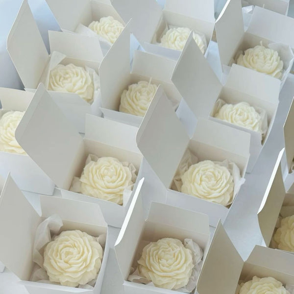 Set of 10 cream-colored peony flower candles in white open boxes arranged in rows.