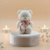 White teddy bear with a red ribbon on a beige background with candles and flowers.
