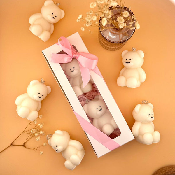 Boxed set of six small cream-colored teddy bear candles with smooth texture and simple facial details on a peach background.