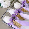 Set of five white tulip-shaped candles tied with lavender satin ribbons and personalized brown tags in clear packaging.