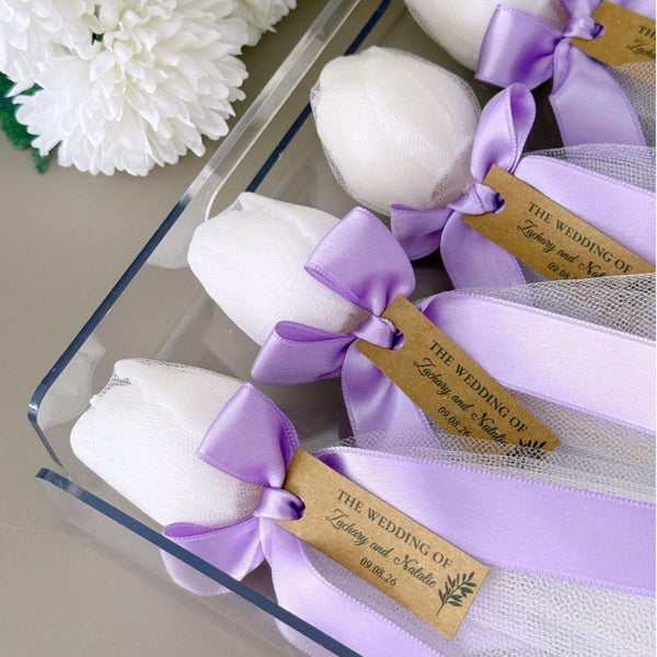 Set of five white tulip-shaped candles tied with lavender satin ribbons and personalized brown tags in clear packaging.