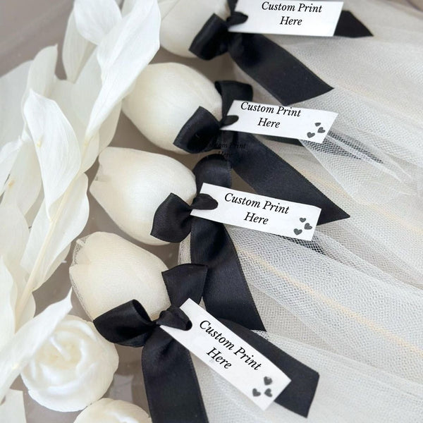 Set of five white tulip-shaped candles wrapped in sheer fabric with black ribbon and customizable tags.