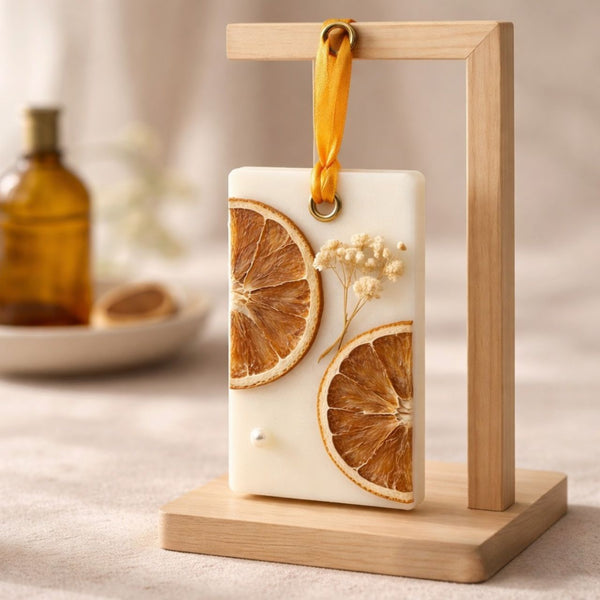 Rectangular white soy wax sachet with dried orange slices and flowers, hanging on a wooden stand with a yellow ribbon.