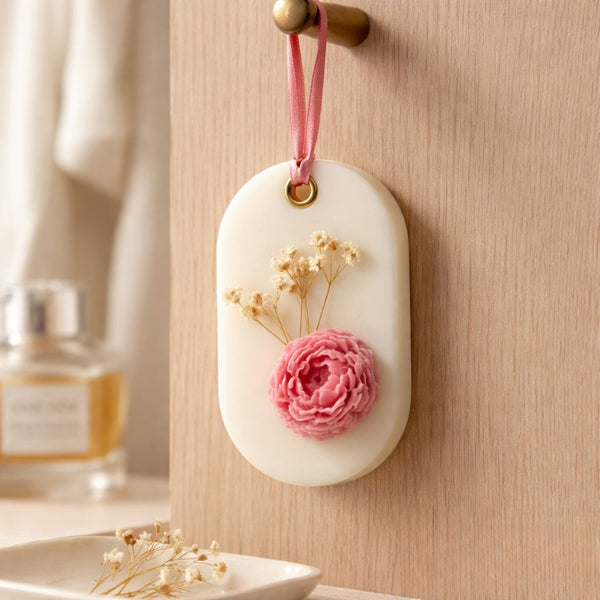 Oval white soy wax sachet with pink flower and dried white blossoms, hanging on wooden knob.
