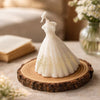 White bridal wedding dress-shaped candle with gold detailing, displayed on a wooden slice.