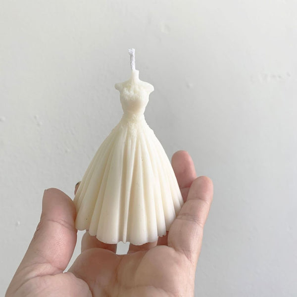 Ivory bridal wedding dress-shaped candle with fitted bodice and full pleated skirt held in hand.
