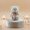 White teddy bear with a red ribbon on a beige background with candles and flowers.