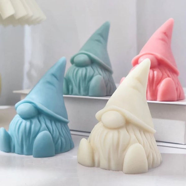 Set of four pastel-colored gnome-shaped soy wax candles in blue, green, white, and pink with detailed beards and hats.