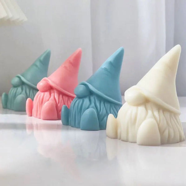Set of four gnome-shaped soy wax candles in cream, blue, pink, and green colors on a white surface.
