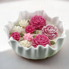 White ceramic candle bowl with scalloped edges holding pink and white floral wax candles.