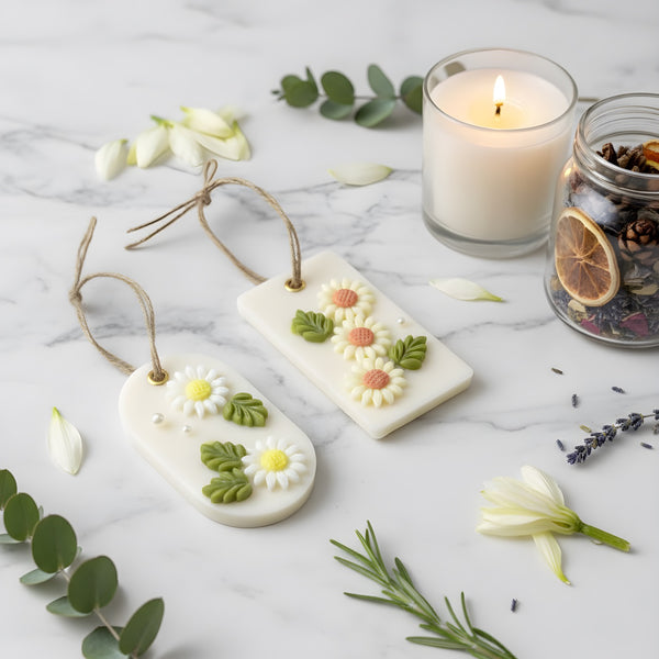 Two white soy wax hanging sachets decorated with dried flowers and leaves, each with a twine loop for hanging, displayed on.