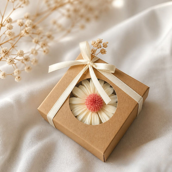 Brown gift box with daisy-shaped candle featuring white petals and a pink center, tied with cream ribbon.