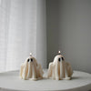 Two white ghost-shaped candles with black eyes lit on a round white surface against a sheer curtain background.