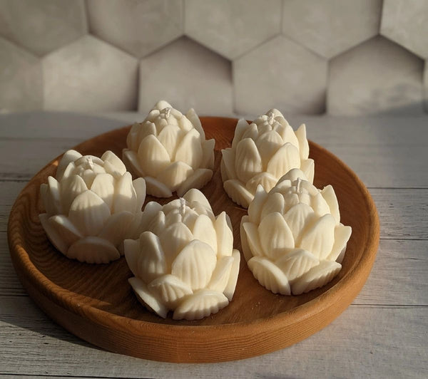 Five white lotus flower-shaped candles arranged on a round wooden tray against a tiled background.